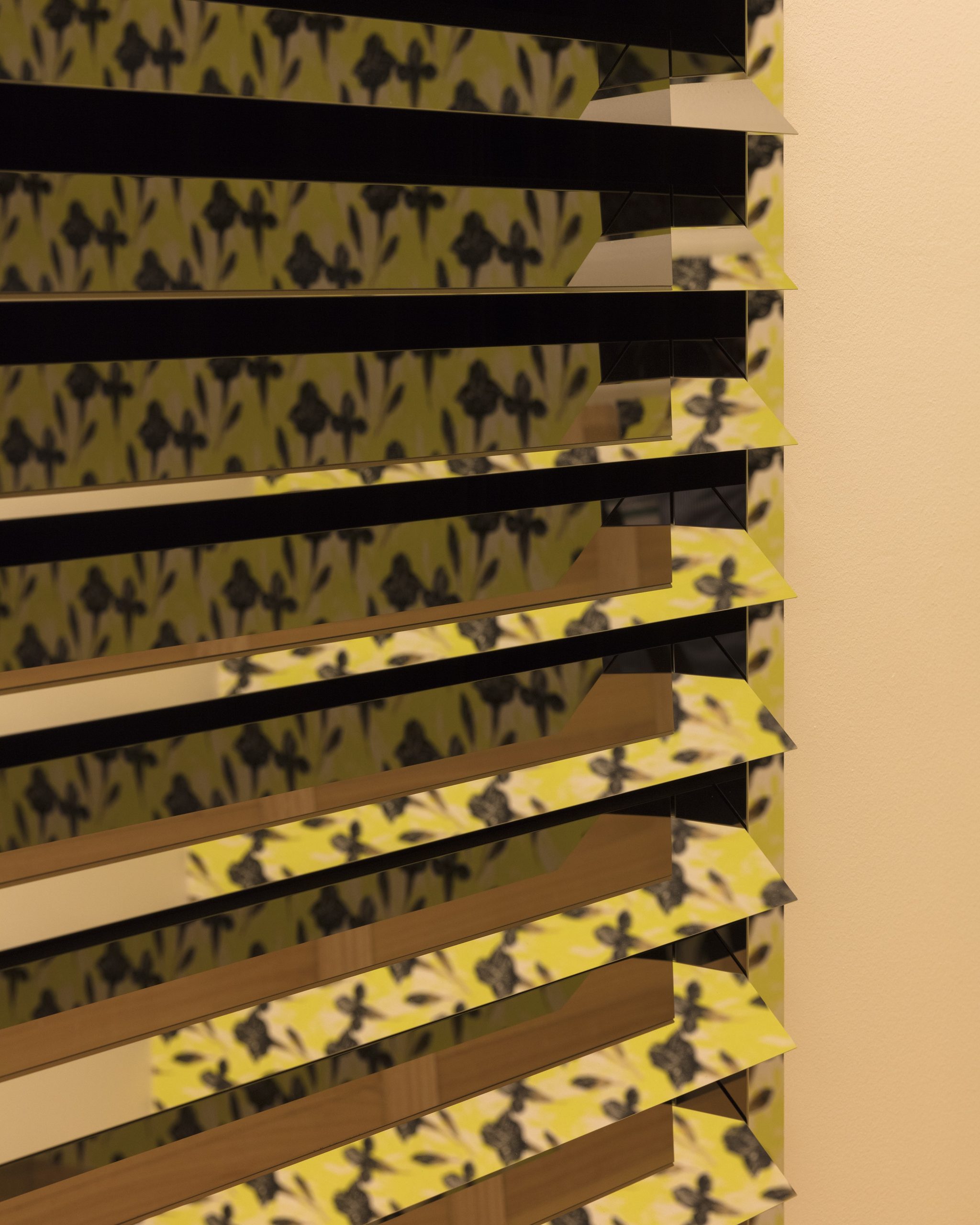 Detailansicht des verspiegelten Shutters mit horizontalen Paneelen vor gelb gemusterter Tapete.